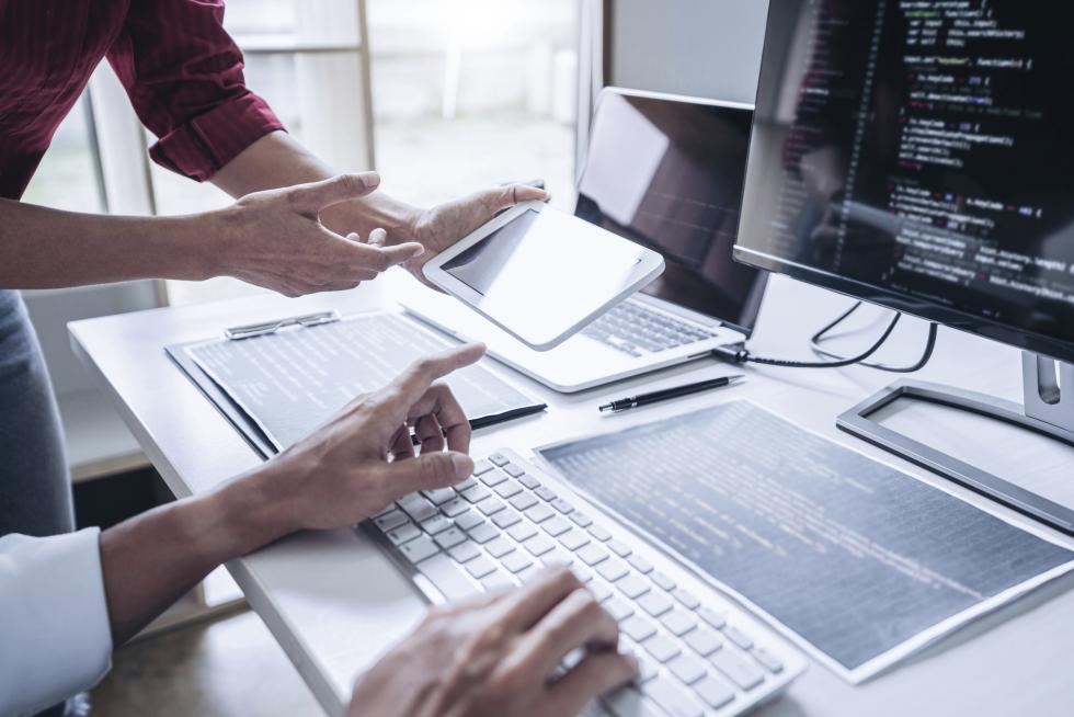 Zwei Personen vor einem Bildschirm mit Laptop und Tablet